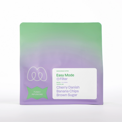 A purple and green gradient bag of Monogram Easy Mode filter coffee, a washed co-fermented blend from Colombia with a Funky Infusions label badge and tasting notes of cherry danish, banana chips, and brown sugar.