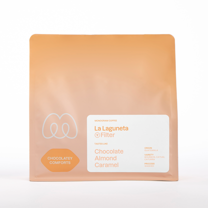 A peach-colored bag of Monogram La Laguneta filter coffee, a washed Bourbon, Catuai, and Caturra variety from Guatemala with tasting notes of chocolate, almond, and caramel.
