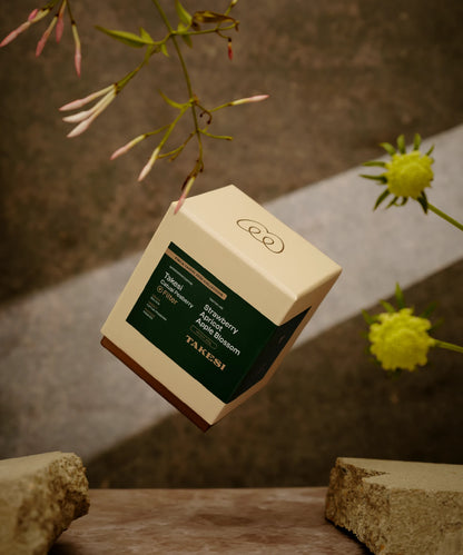 A cream and dark forest green box of Monogram Takesi Catuai Peaberry filter coffee floating in mid-air, a washed specialty coffee from Bolivia with tasting notes of strawberry, apricot, and apple blossom.