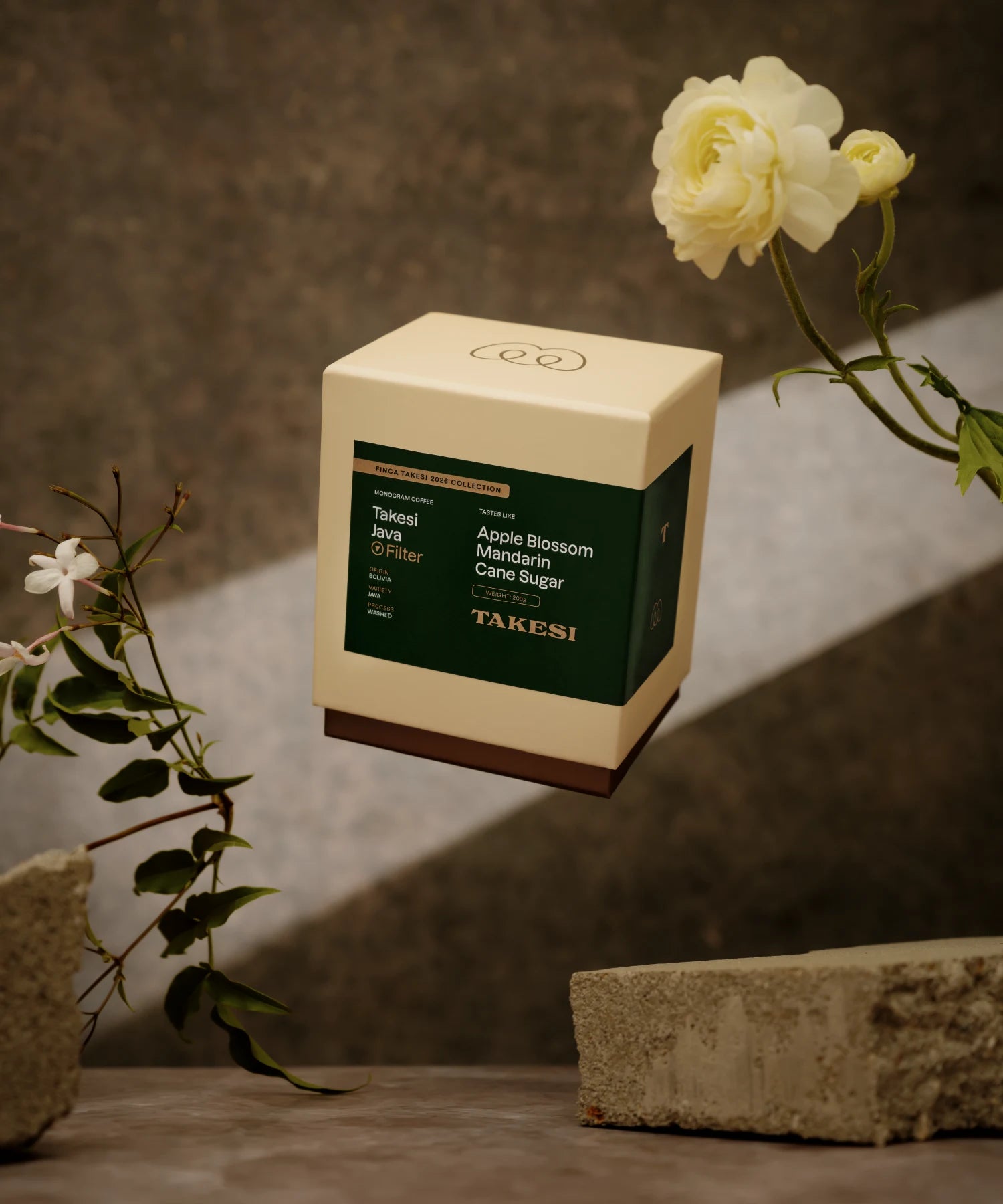 A cream and dark forest green box of Monogram Takesi Java filter coffee floating in mid-air, a washed specialty coffee from Bolivia with tasting notes of apple blossom, mandarin, and cane sugar.
