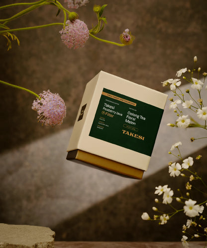 A cream and dark forest green box of Monogram Takesi Peaberry Java filter coffee floating in mid-air, a washed specialty coffee from Bolivia with tasting notes of oolong tea, floral, and melon.