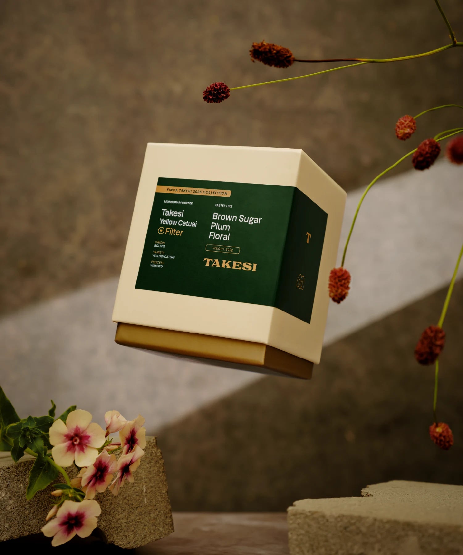A cream and dark forest green box of Monogram Takesi Yellow Catuai filter coffee floating in mid-air, a washed specialty coffee from Bolivia with tasting notes of brown sugar, plum, and floral.